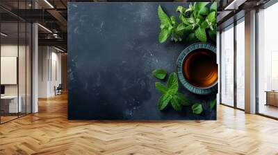 A tranquil image of a cup of herbal tea with fresh green mint leaves placed on a dark slate background. The contrast between the green mint and dark background highlights the freshness and health Wall mural