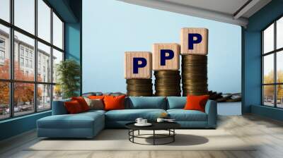 PPP - acronym on wooden cubes. Which stand on stacks of coins on a light background Wall mural