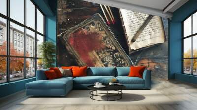 Two antique books with intricate covers and an old pen lie on a rustic wooden table, surrounded by matches. The aged pages and worn surfaces evoke a sense of history and nostalgia. Wall mural