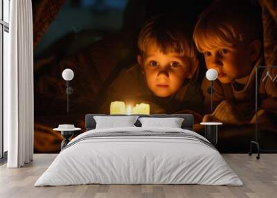 Two young boys lie under a blanket, captivated by the flickering light of a candle. The cozy setting creates a warm and serene atmosphere, ideal for bedtime stories and quiet moments. Wall mural