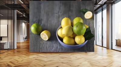 Fresh ripe lemons and limes in blue bowl on gray wooden table. Wall mural