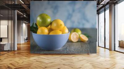 Fresh ripe lemons and limes in blue bowl on gray wooden table. Wall mural