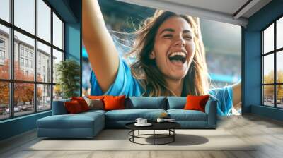 An excited young beautiful woman fan wearing a sport shirt cheered at the football stadium, cheering for their team to win the game. Wall mural