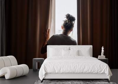 Woman opening curtains in sunlit room. Concept of morning routine. Wall mural