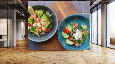 Two plates of vegetable salad with feta cheese, cucumbers, tomatoes, and broccoli served in bowl on rustic wooden board. Wall mural