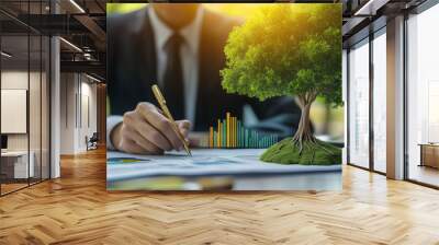 A businessman using a calculator and analyzing financial data at his desk with a small growth tree concept symbolizing green business and environmental sustainability. The setup reflects the harmony b Wall mural