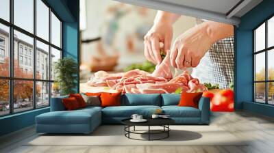 Close-up of hands skillfully preparing fresh ingredients for a traditional Italian meal, featuring prosciutto, leafy greens, and vibrant vegetables on a rustic table. The scene captures the essence of Wall mural