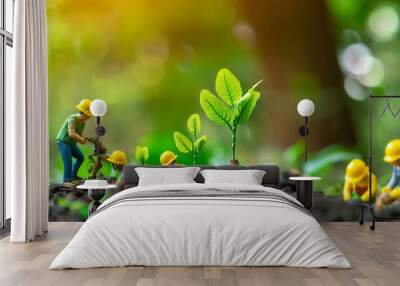 Miniature workers planting tree seedlings in soil with hard hats, nature conservation concept. Focus on tiny people cultivating green plants with blurred natural background, representing teamwork, sus Wall mural