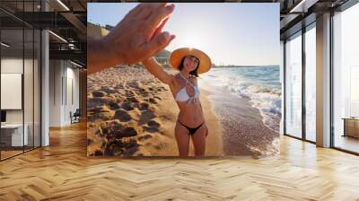 beautiful girl in a hat and bikini gives her friend a high five. Meeting with friends while traveling along the seashore. Wall mural