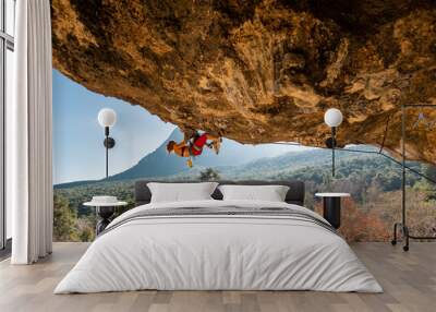 Girl climber on an overhanging rock. A sports woman climbs a rock against the backdrop of mountains. difficult movements in rock climbing. Wall mural