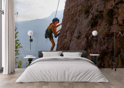 The child is climbing on a natural terrain. A boy climbs a rock on a background of mountains. Extreme hobby. Rock climbing safety.. Wall mural