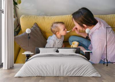 Mom feeds a small child at home with yogurt from a spoon. Family concept Wall mural