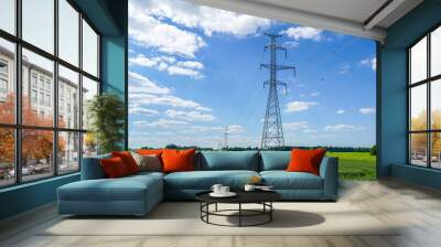 High-voltage power transmission line pylons in a crop field, blue sky and white clouds Wall mural