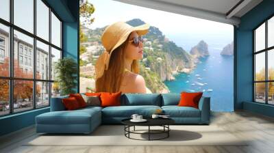 Attractive fashion woman with sunglasses and straw hat enjoying Capri sight from terrace, Capri Island, Italy Wall mural