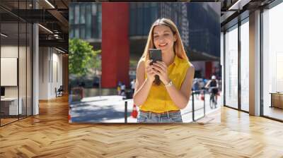 Brazilian girl using mobile phone app for chat on sunny day in Paulista Avenue, Sao Paulo, Brazil Wall mural