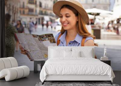 Happy young woman with a city map, straw hat and backpack travelling Wall mural