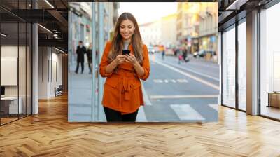 Portrait of beautiful smiling woman walking in city street texting on mobile phone with blurred background Wall mural