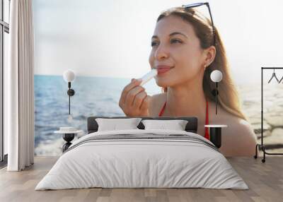 Smiling young woman applying sun protection on her lips on the beach Wall mural