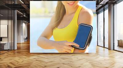 Sport armband for smartphone. Sporty girl touching her smart phone before outdoor fitness workout at the beach. Wall mural