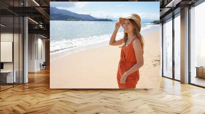 Summer holidays on the beach. Young woman with orange sundress and straw hat smiling relaxed on the sand beach. Wall mural