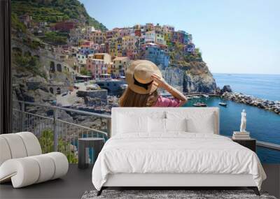 Traveler girl enjoying vacations in Italy. Young woman wearing hat and dress looking at italian village of Manarola with sea. Wall mural