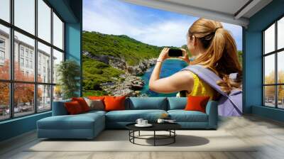 Young hiker girl taking photo with smartphone of natural tropical landscape. Wide angle. Wall mural