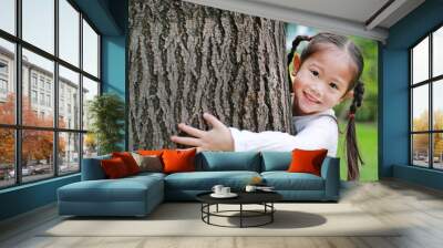 Close up of a smiling child girl embracing tree at the garden. Wall mural