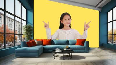 Happy attractive young Asian little girl pointing two index finger up beside on yellow isolated background with clipping path Wall mural