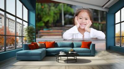 Happy little Asian kid girl lying on the wooden table with looking camera. Wall mural