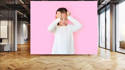 Little asian girl suffering from headache desperate and stressed because pain isolated on pink background. Kid with hands on head Wall mural