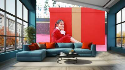 Little child girl in red dress poses sitting near a big gift in winter season and happy new year festival against christmas background. Wall mural