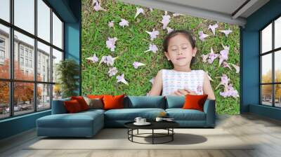 Pretty little girl sleeping on green grass with fall pink flower in the garden outdoor. Wall mural