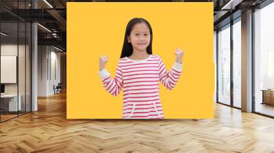 Smiling asian little girl raising hands up and gesture strong. Portrait of happy child isolated on yellow background with clipping path. Good health concept Wall mural