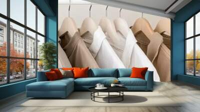 A neat wardrobe displays various beige sweaters hanging on wooden hangers, set against a calming beige background that enhances the clean look Wall mural