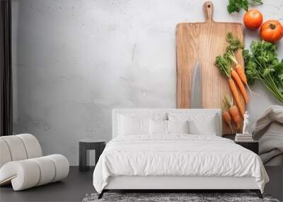 A wooden cutting board with three whole carrots, green tops, and a silver knife. Some chopped carrots are scattered on the board and the counter. Wall mural