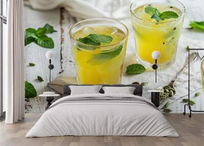 yellow cardamom milk on a white wooden background, featuring two glasses filled with the drink and garnished with mint leaves near a cut spoon. Wall mural