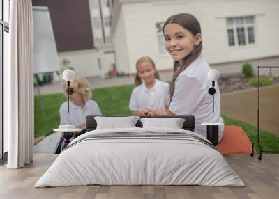 A girl in white shirt sitting at the lesson and smiling Wall mural