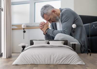 A gray-haired man sitting on the floor and looking thoughtful Wall mural