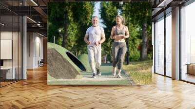 A mature couple running in the park and looking contented Wall mural