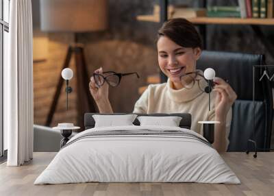 A young woman holding two pairs of eyeglasses and smiling Wall mural