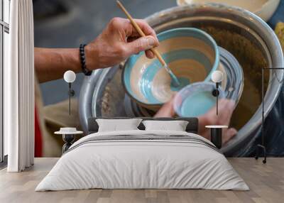 Closeup of woman painting clay mug, coloring pottery in workshop with a paintbrush. Wall mural