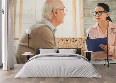 Confident dark-haired woman in clear glasses talking to old man Wall mural