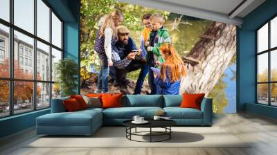 Eco energy. Positive bearded man sitting in front of children while showing them solar battery model Wall mural