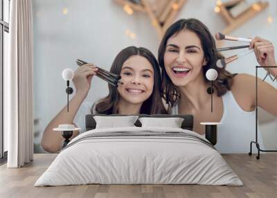 Enthusiastic mom and daughter showing makeup brushes Wall mural