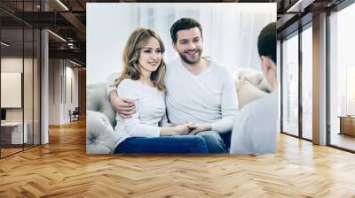 Family reunion. Delighted pleasant happy couple holding each other hands and being thankful to their therapist for psychological sessions while sitting together on the sofa Wall mural