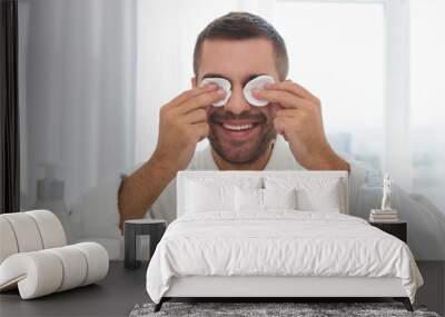 Fresh look. Positive handsome man putting cotton pads on his eye while wanting to look fresh Wall mural