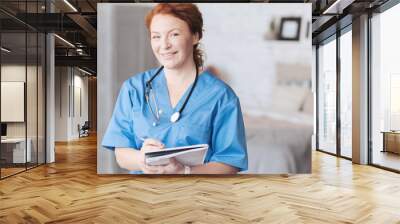 Friendly looking nurse with notebook smiling into camera Wall mural