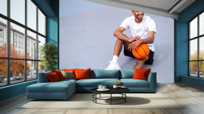 Man in sports wear sitting on the floor and holding a ball in hands Wall mural