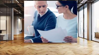 Mature businessman looking at papers brought by young employee Wall mural