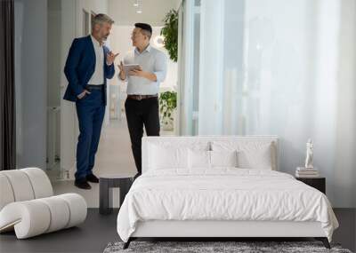 Men standing in corridor in office and talking about their work. Wall mural